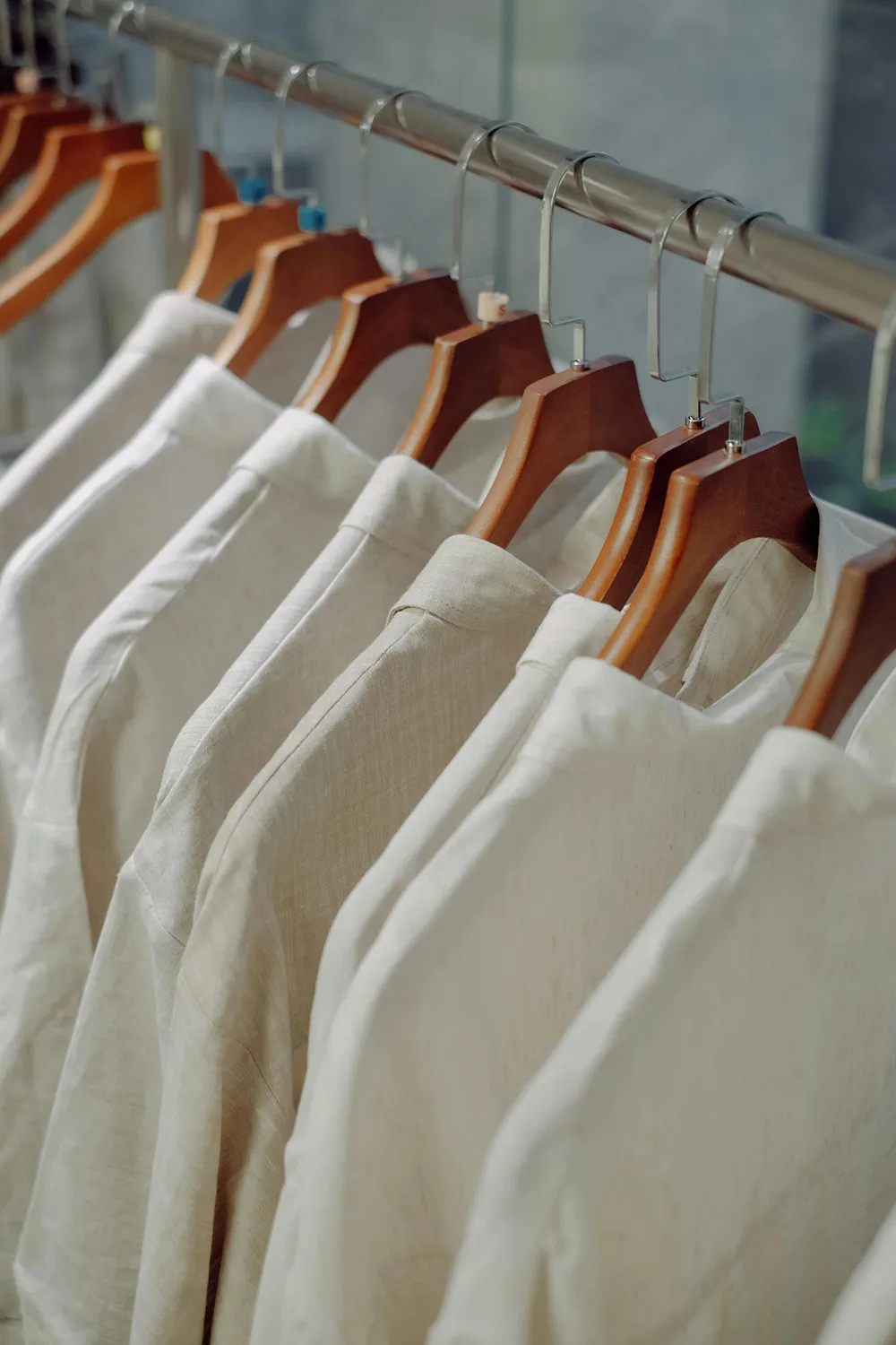 เสื้อเชิ้ตผ้าลินินสีขาวแขวนเรียงบนราวไม้ ให้ความรู้สึกเรียบง่ายและเป็นธรรมชาติ